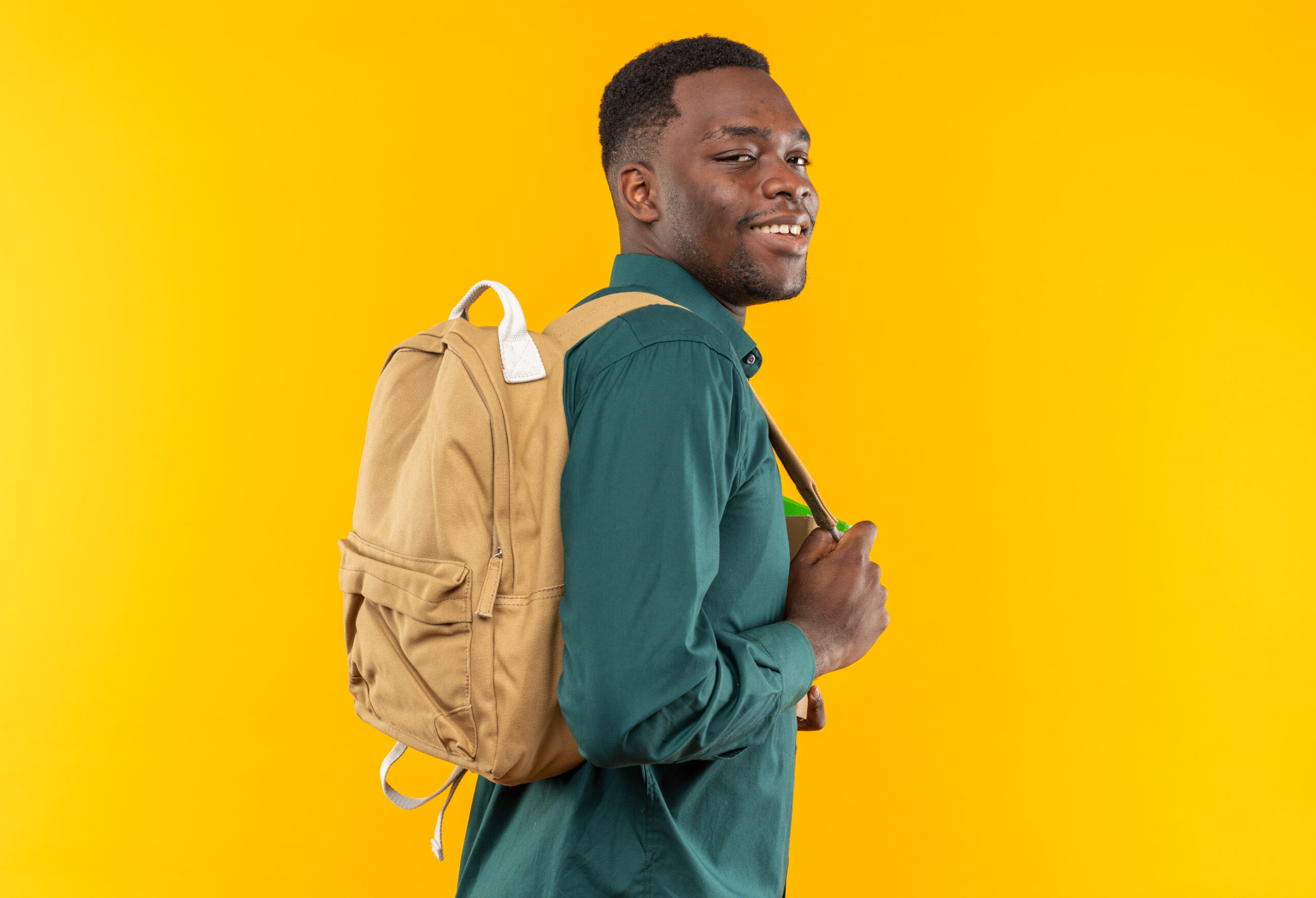smiling young afro-american student with backpack standing with his back to camera isolated on orange background with copy space